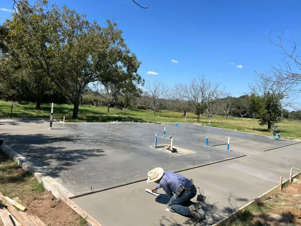 A man is kneeling on the ground working on a concrete driveway.