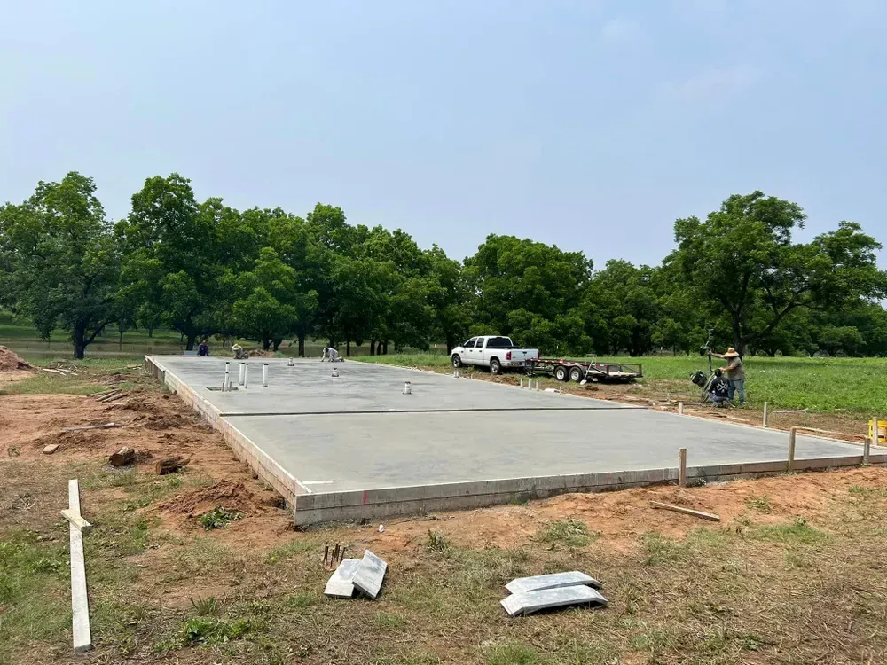 A concrete foundation is being built in a field with trees in the background.