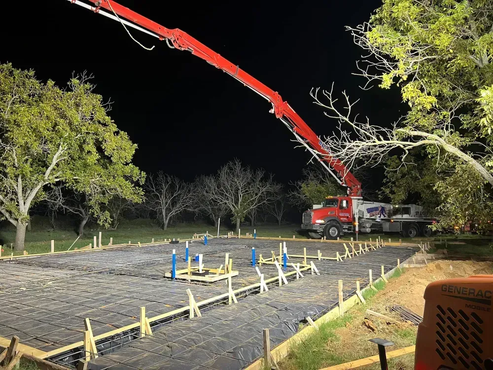 A crane is pouring concrete on a construction site at night.