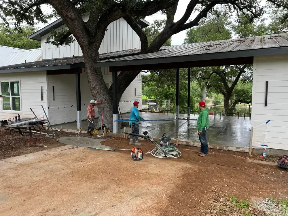 Two men are working on a concrete floor in front of a house.