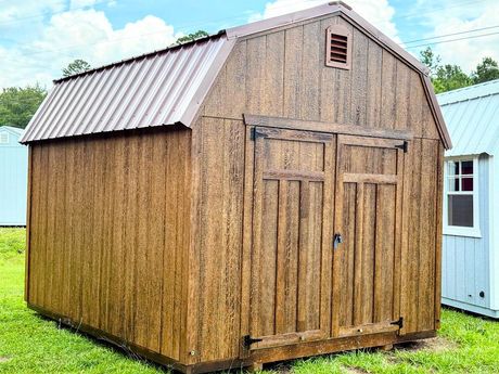 A gray and white shed with a window and doors is sitting in the grass.