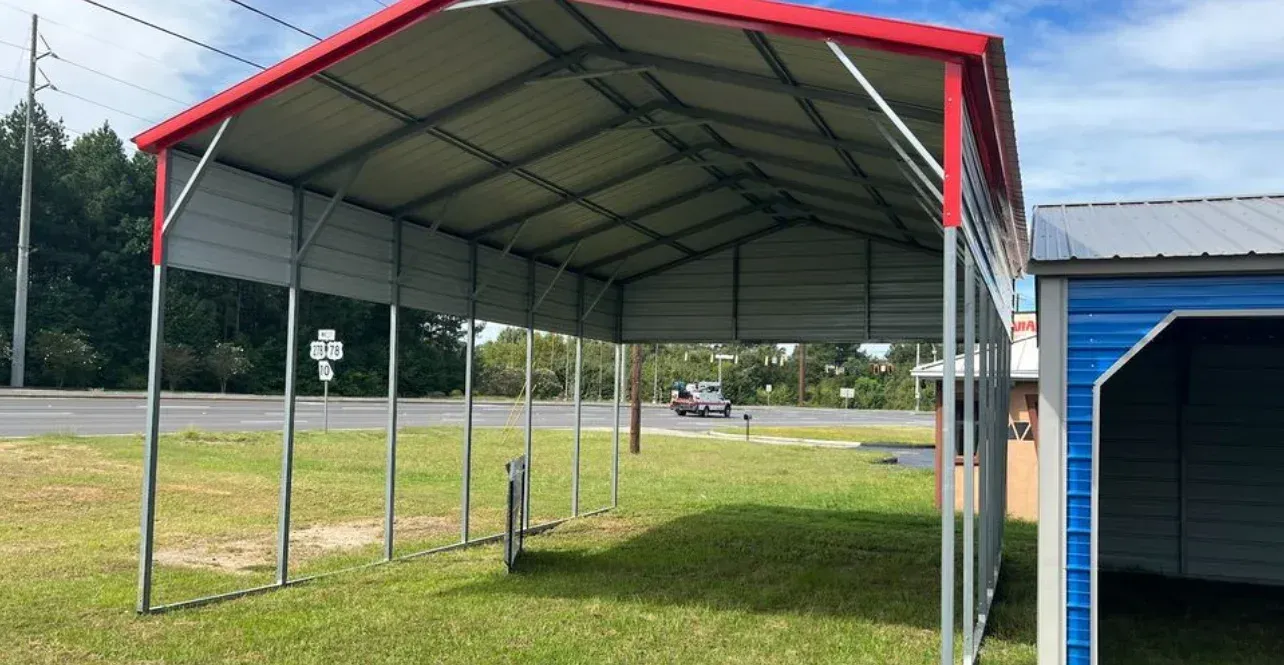 A red and white carport is sitting in the middle of a grassy field.