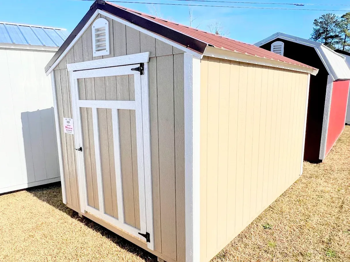 A small wooden shed with a red roof is sitting in a field.