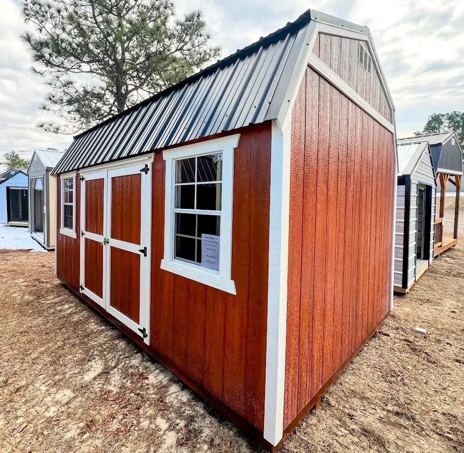 A wooden shed with a window and a metal roof is sitting in the dirt.
