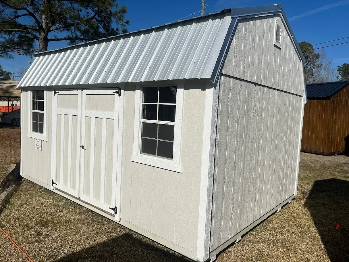 A white shed with a metal roof is sitting on top of a dirt field.