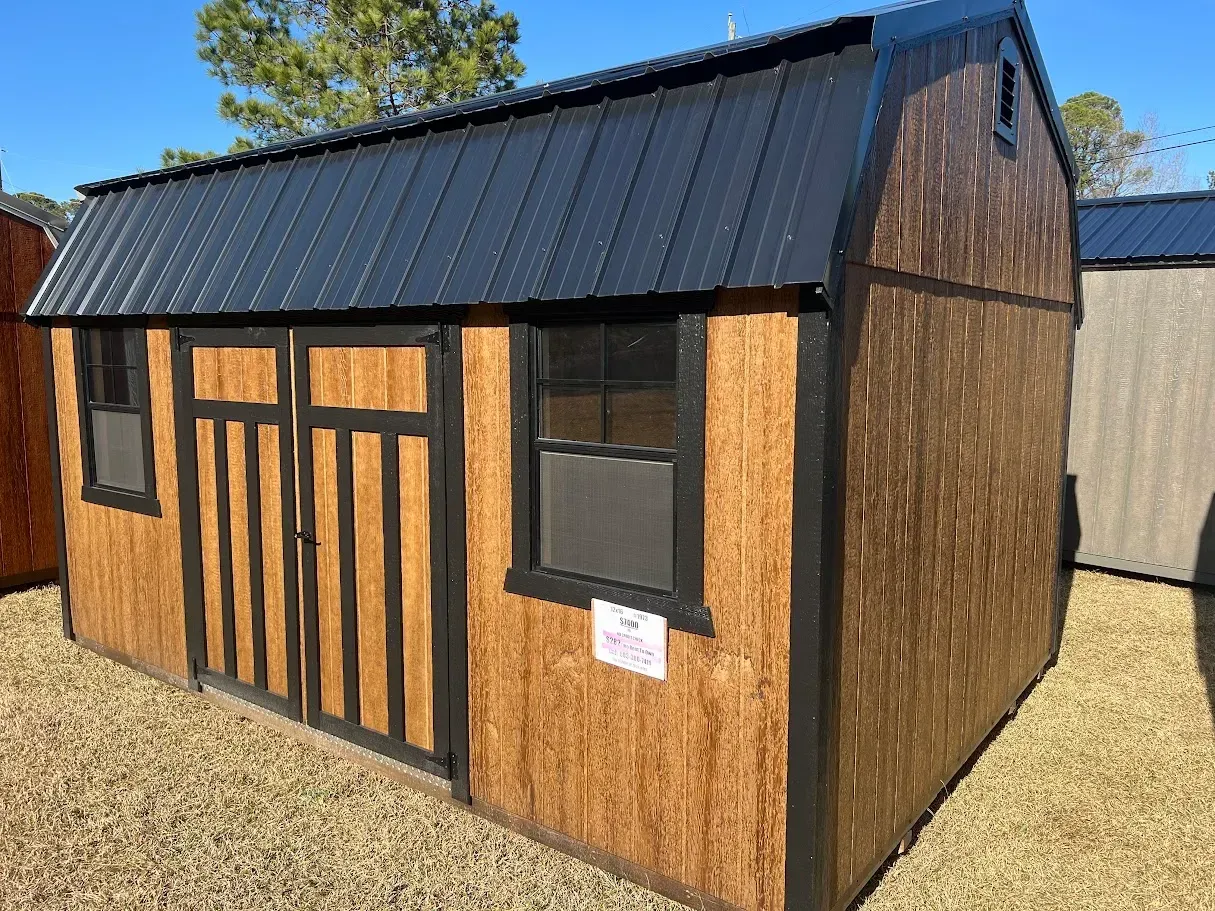 A wooden shed with a black roof is sitting on top of a dirt field.