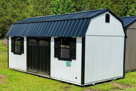 A gray and white shed with a window and doors is sitting in the grass.