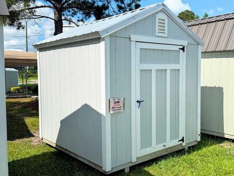 A gray and white shed with a window and doors is sitting in the grass.