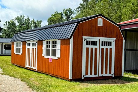 A gray and white shed with a window and doors is sitting in the grass.
