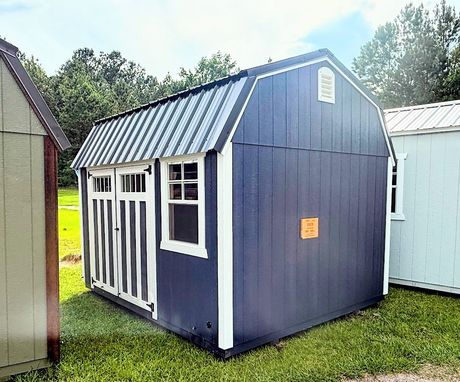 A gray and white shed with a window and doors is sitting in the grass.