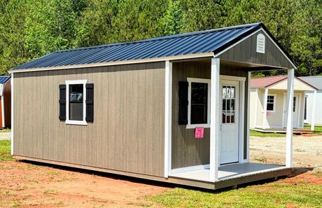A gray and white shed with a window and doors is sitting in the grass.