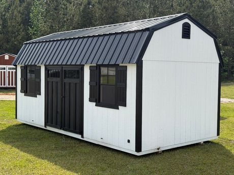A gray and white shed with a window and doors is sitting in the grass.