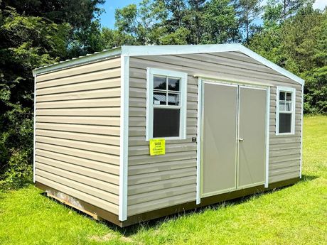 A gray and white shed with a window and doors is sitting in the grass.
