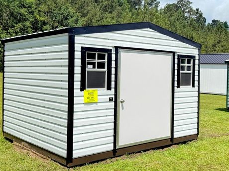 A gray and white shed with a window and doors is sitting in the grass.