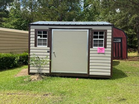 A gray and white shed with a window and doors is sitting in the grass.
