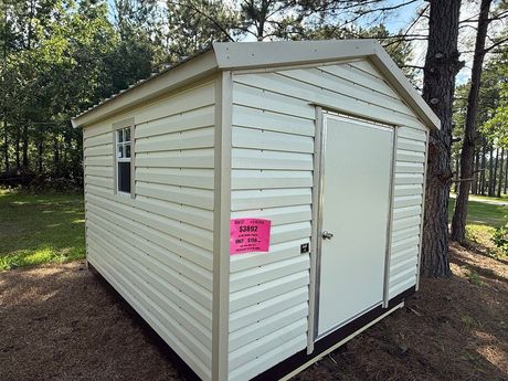 A gray and white shed with a window and doors is sitting in the grass.