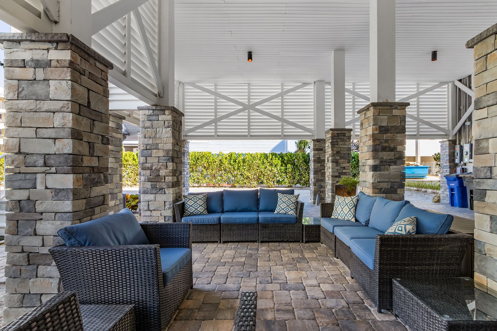 Covered patio with wicker seating, blue cushions, stone columns, and a white roof.