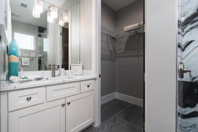 Bathroom with white vanity, walk-in closet, and marble shower door.