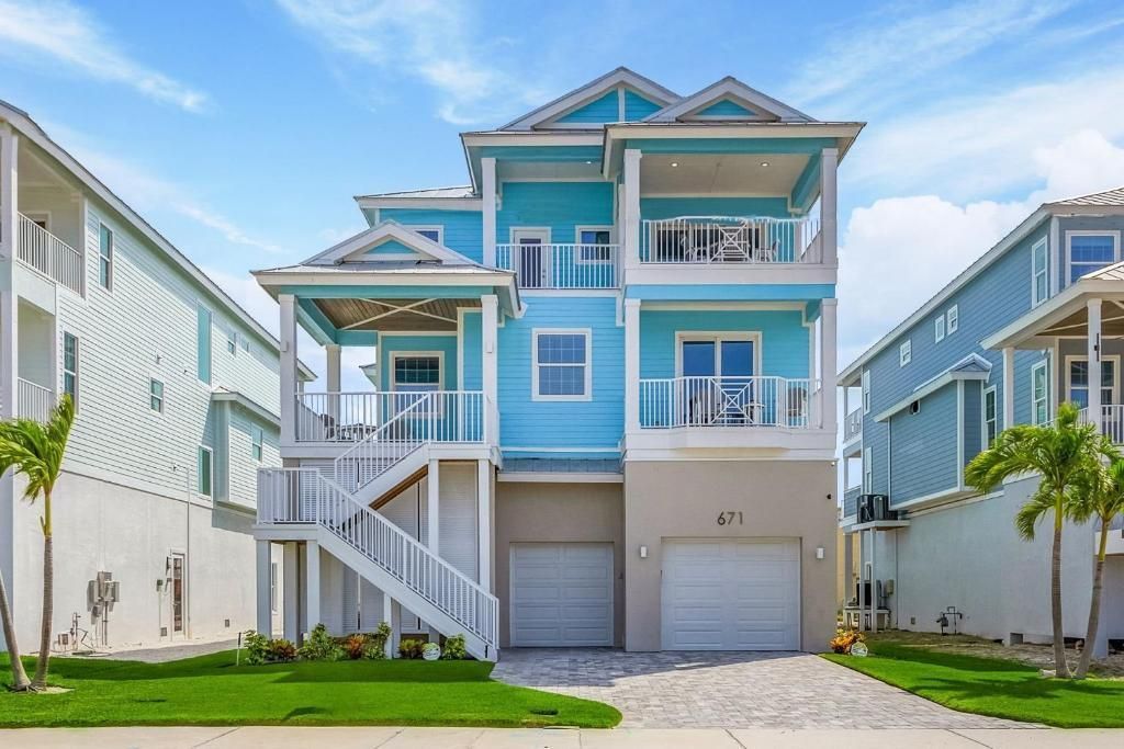 Multi-story blue beach house with balconies, garage, and palm trees.