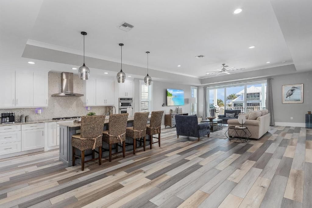 Modern open-concept kitchen and living room with island seating, hardwood floors, and large windows with a view.