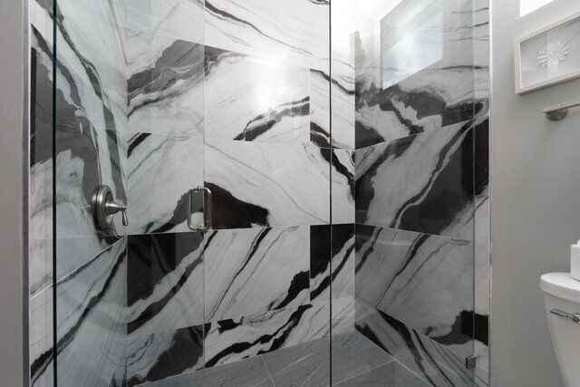 Shower with marble-patterned black and white tiles, glass doors, and silver fixtures.
