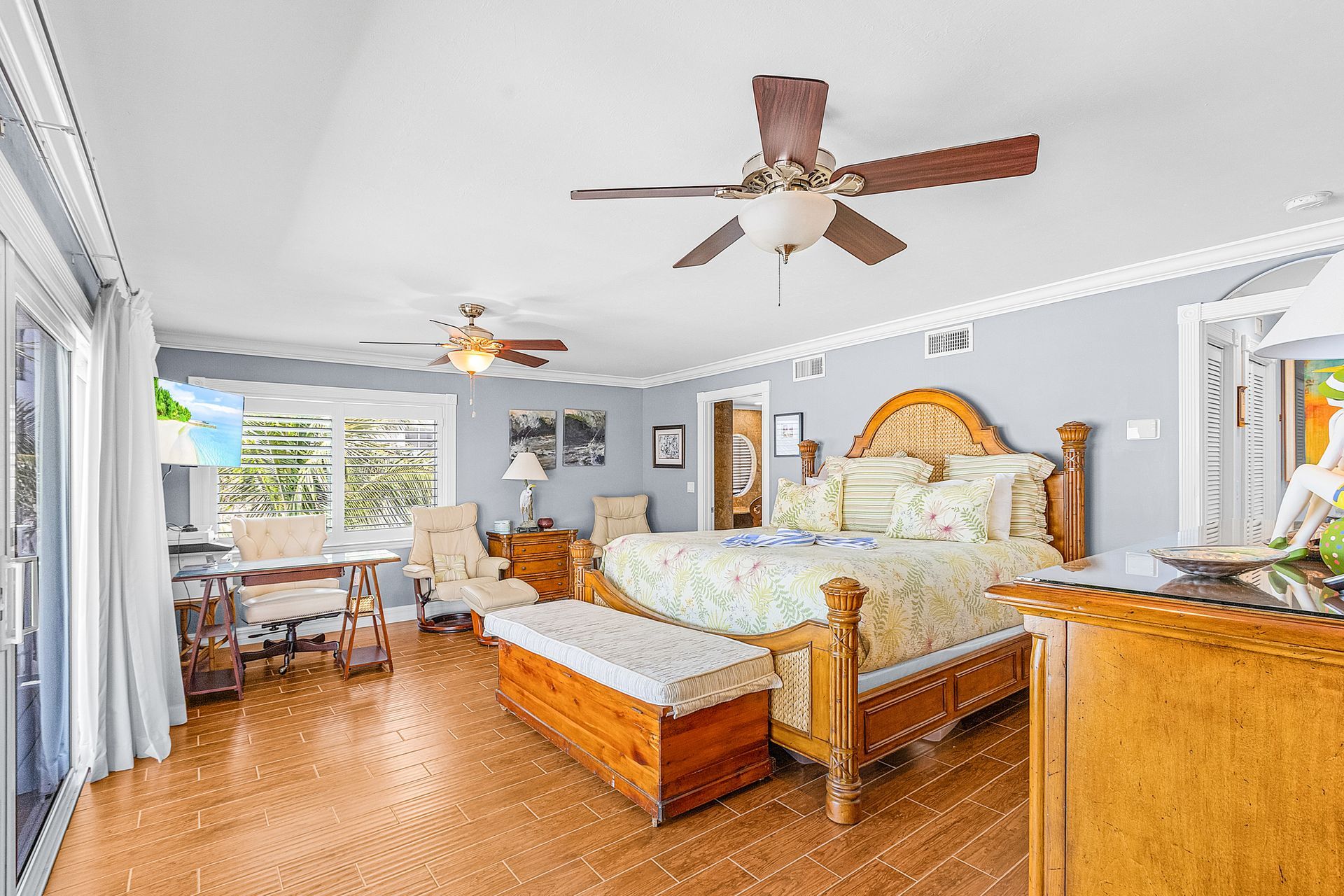Bright bedroom with wicker bed, orange bench, ceiling fans, and coastal decor overlooking a dining area