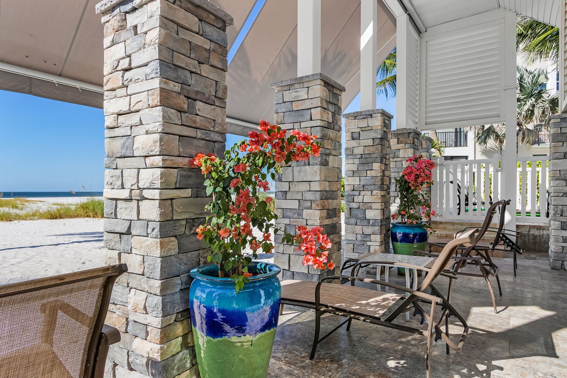 Patio with stone columns, blue planter of red flowers, wicker chairs, and ocean view