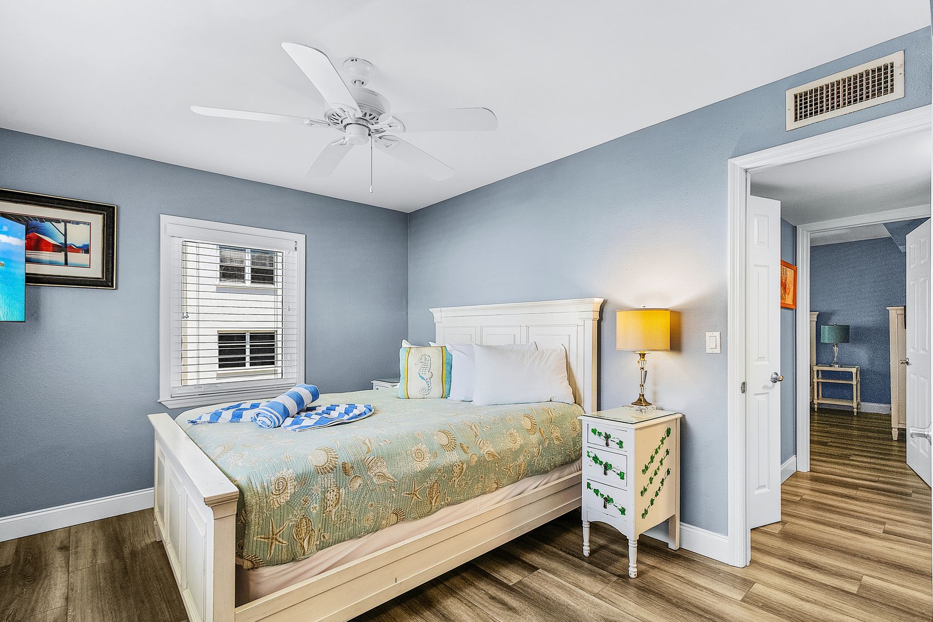 Bright bedroom with a white bed, blue walls, ceiling fan, and open door to a hallway