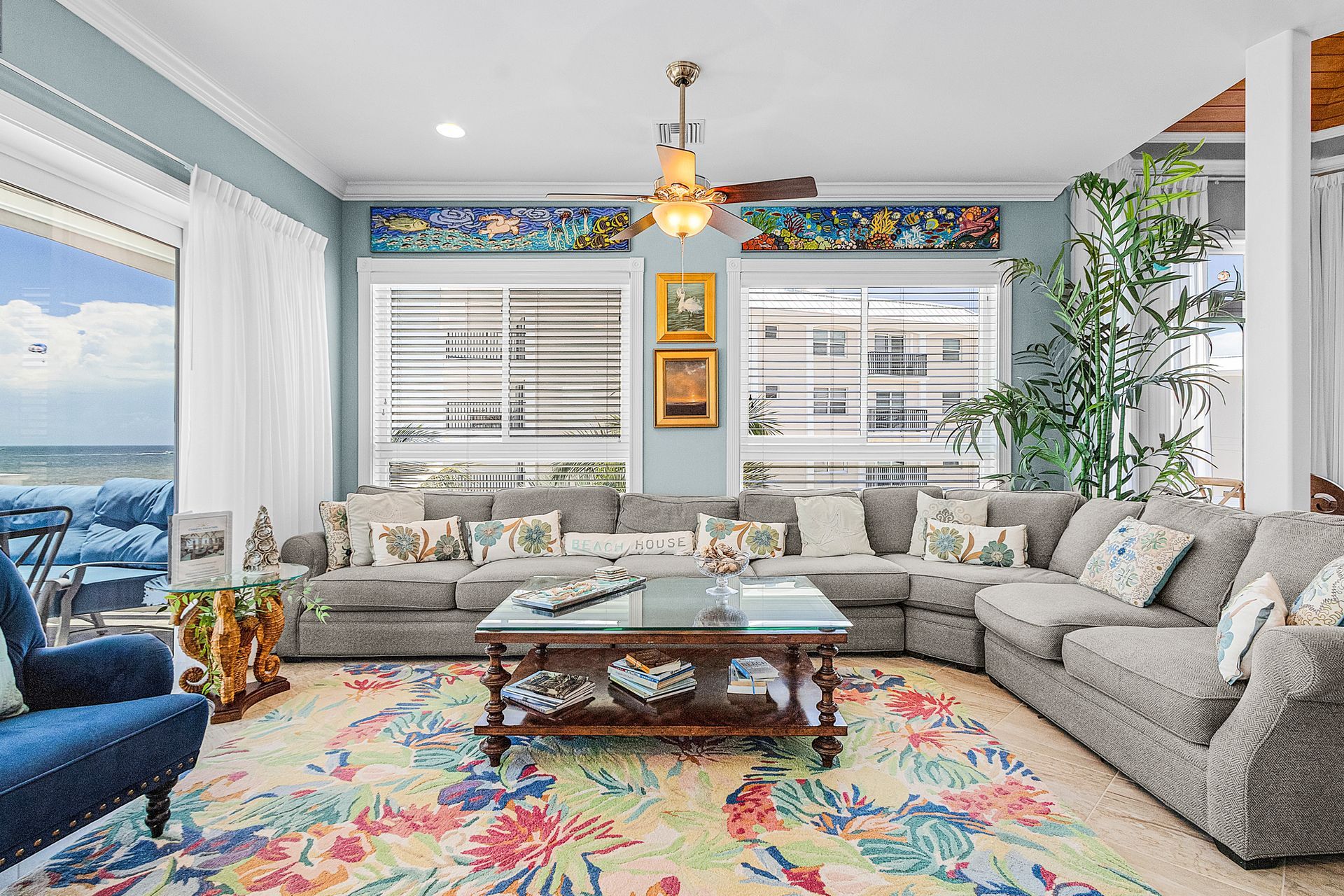 Bright living room with sectional sofa, floral rug, ocean view, and large windows with colorful trim