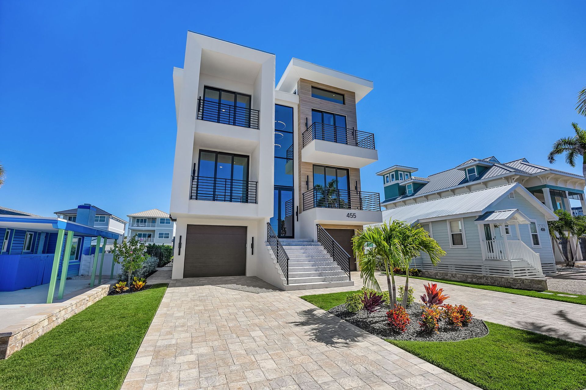 Modern white beachfront house with glass windows and a small palm tree garden.