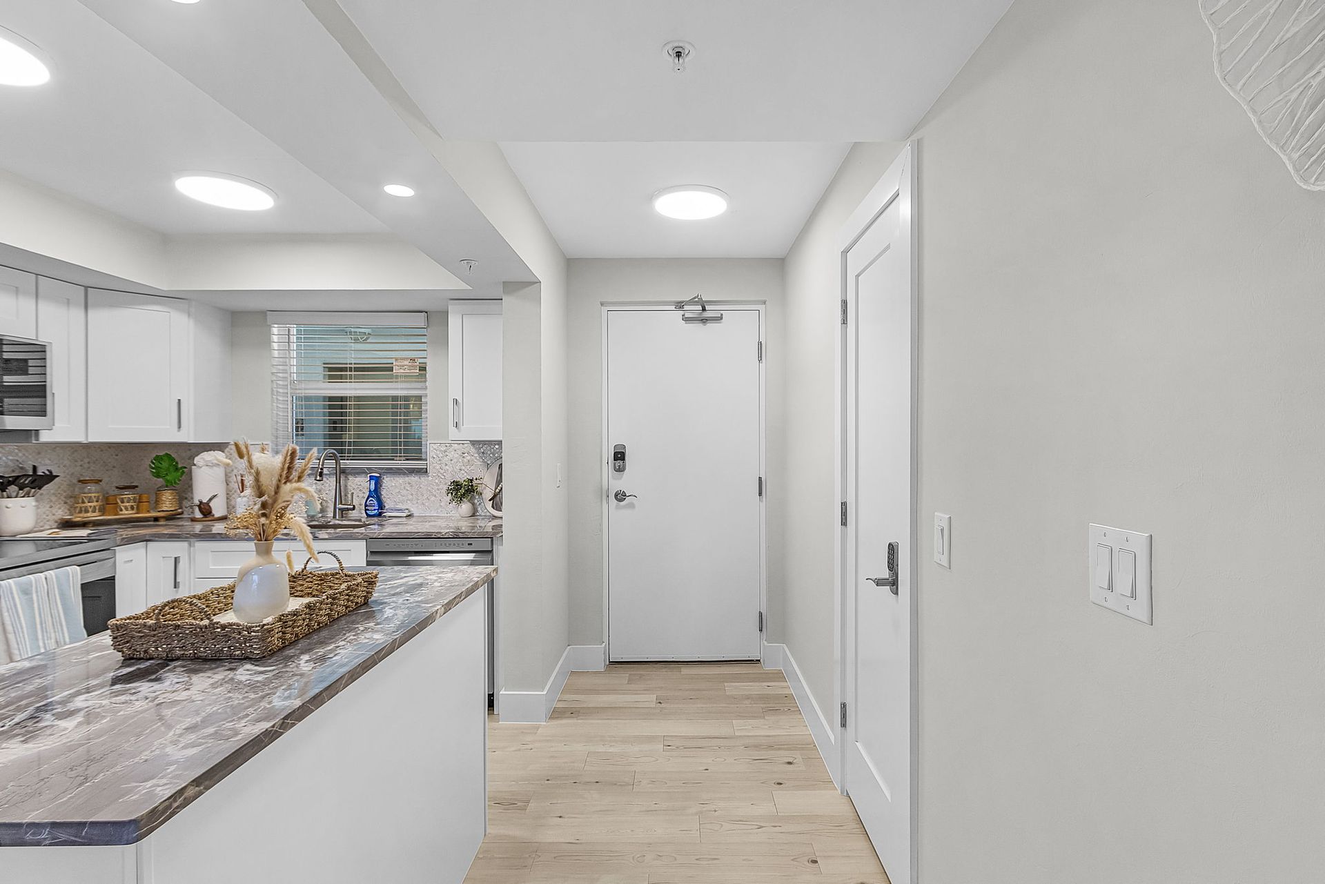 Bright kitchen hallway with a white door, light wood floors, and granite countertop.