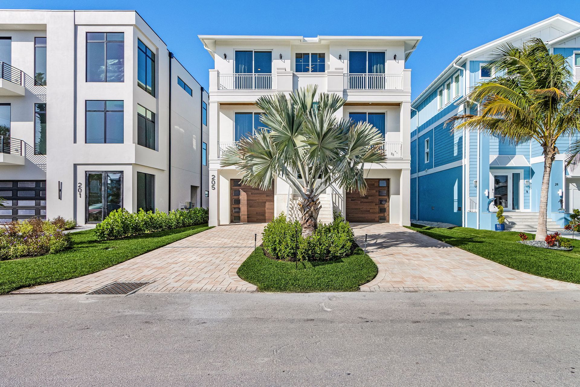 Three-story white house with brown garage doors and balconies; palm tree in front, sunny day.