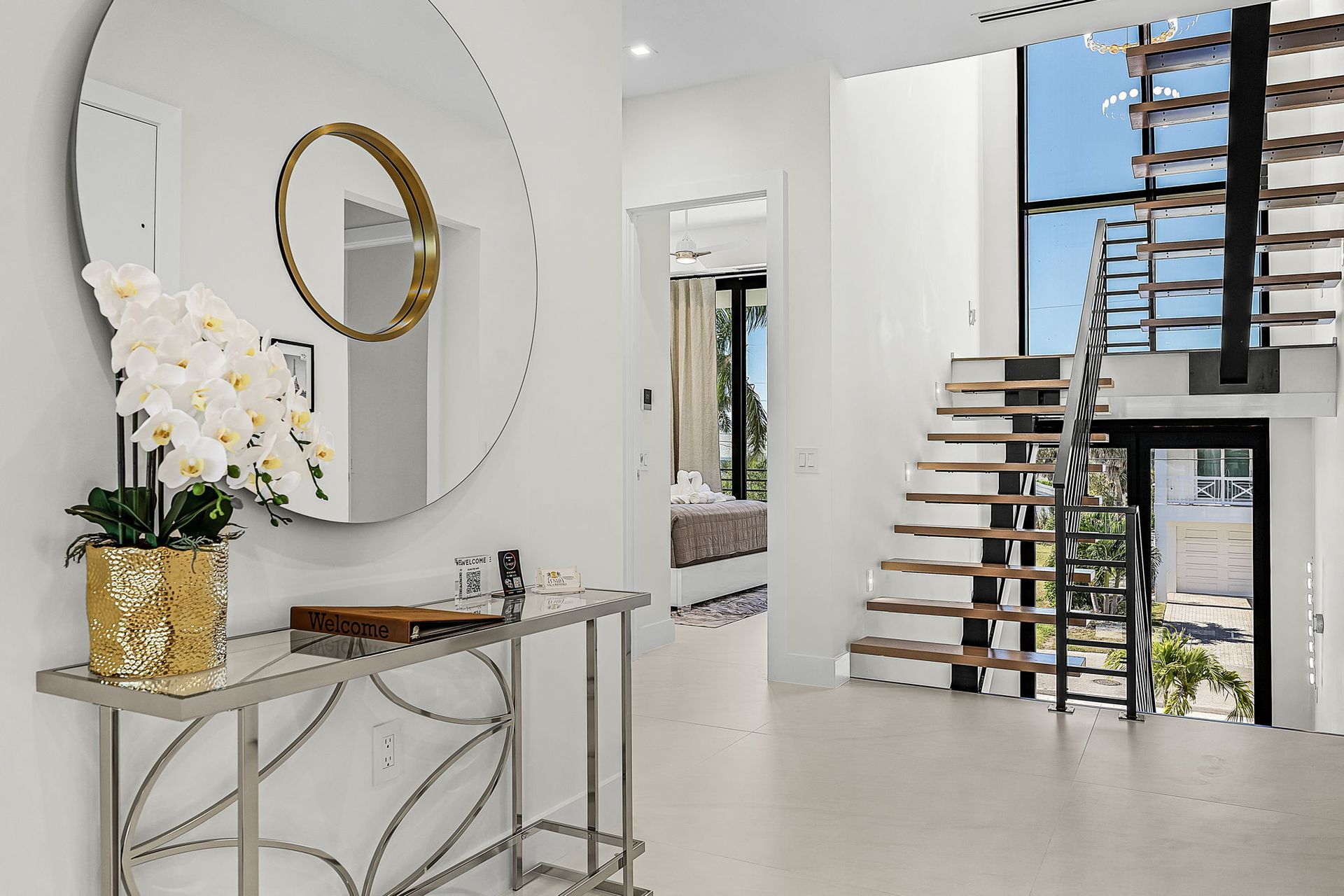 Entryway with a round mirror, console table, staircase, and orchids.