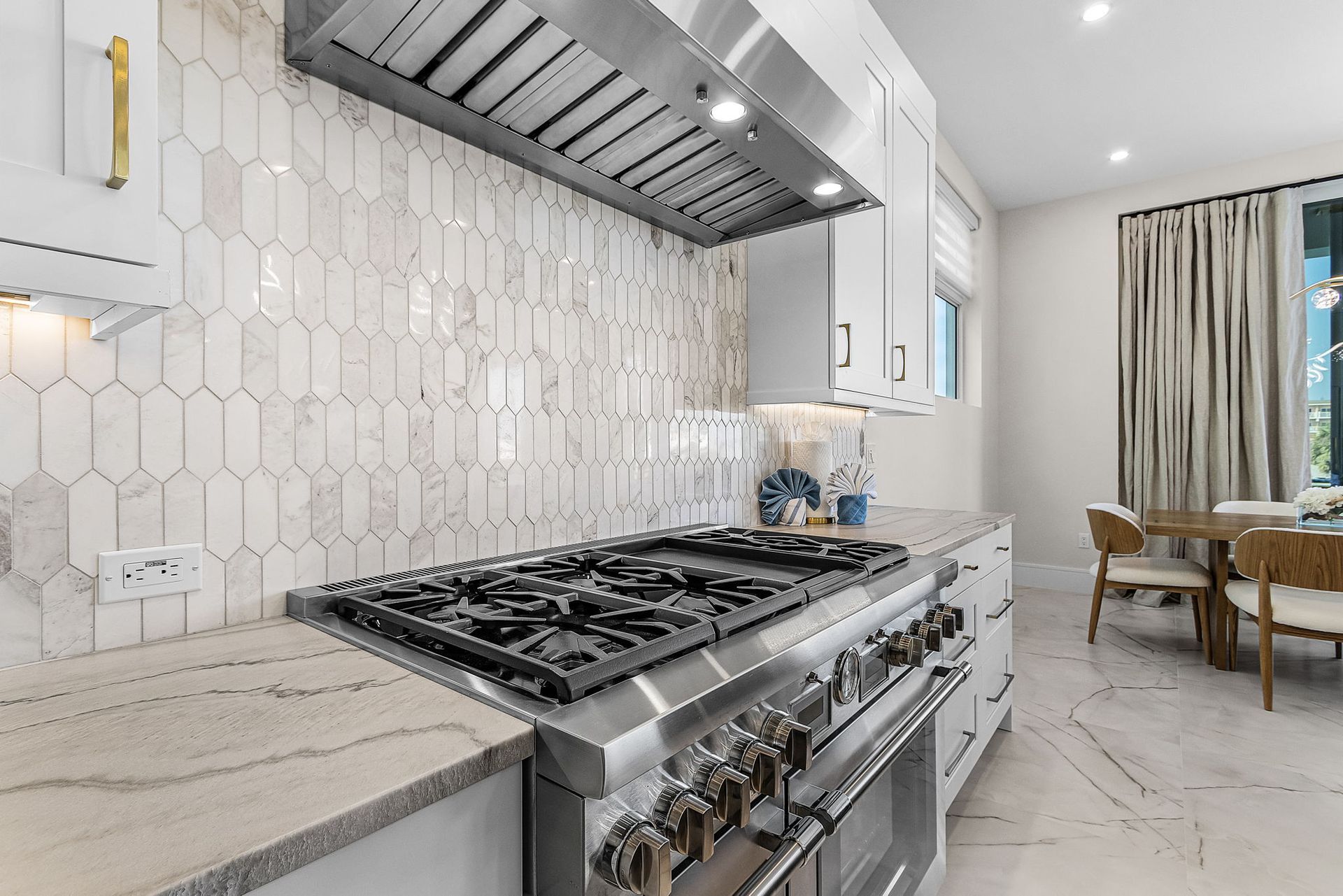 Kitchen with white cabinets, stone countertops, stainless steel range, and tile backsplash.