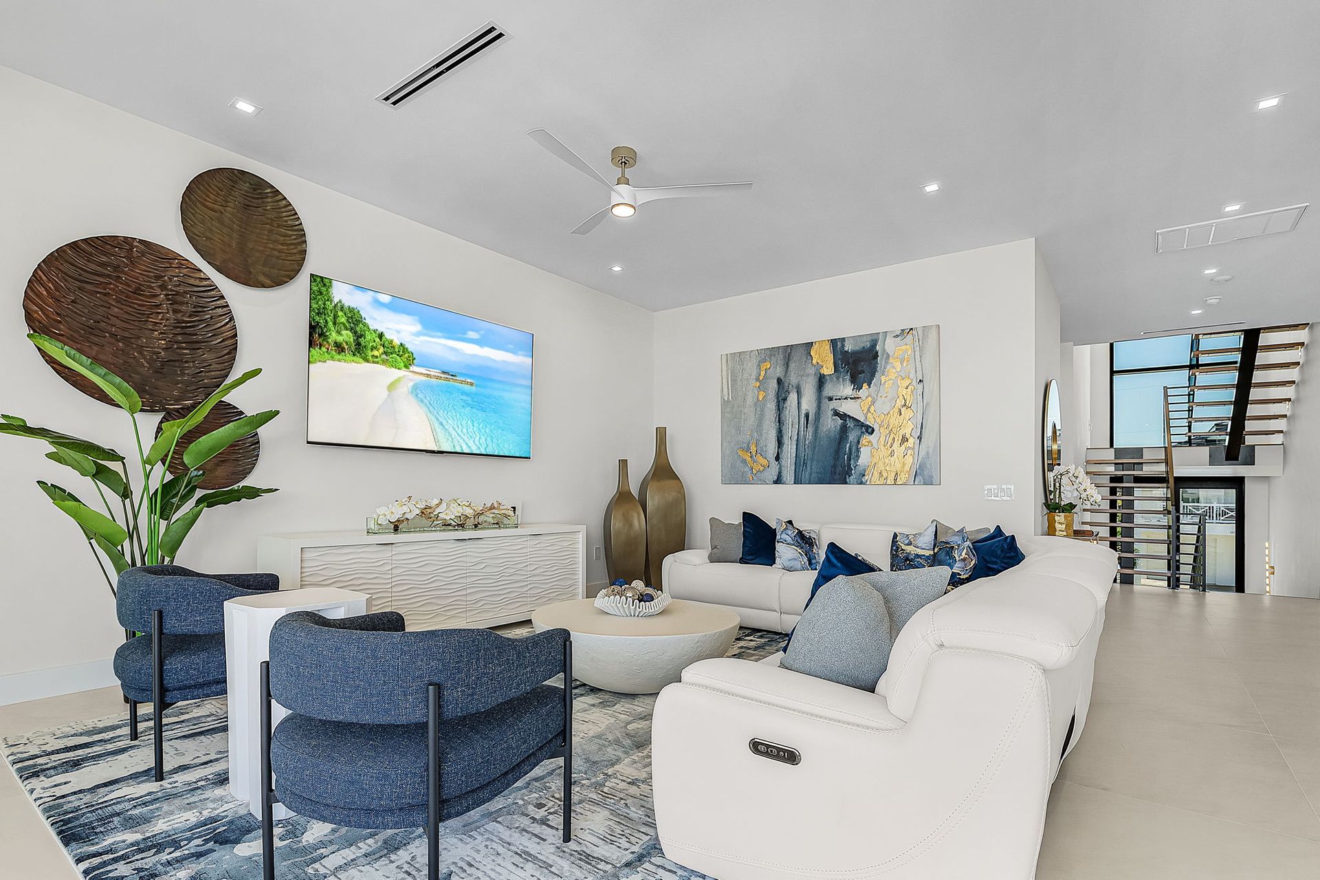 Modern living room with white walls, blue accents, and beach scenery on TV.