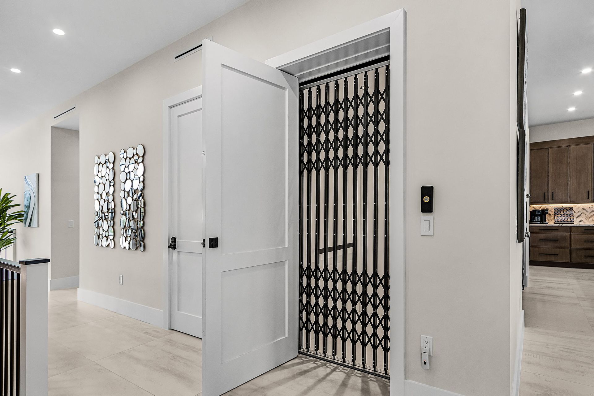 Hallway with a home elevator with a black accordion-style gate and white door.