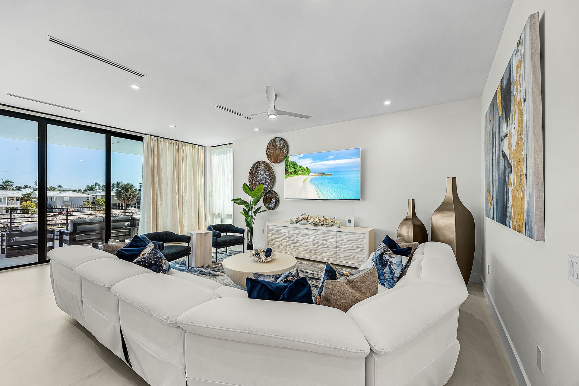Modern living room with white sectional sofa, TV, and large windows overlooking a balcony.