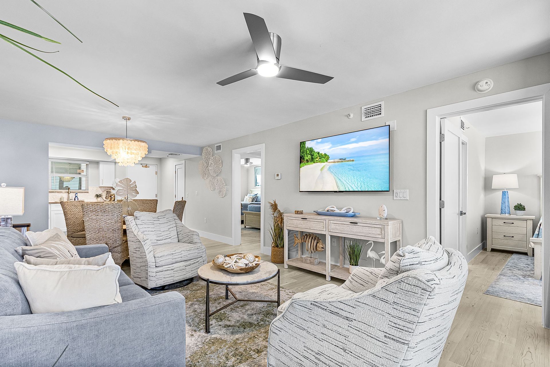 Coastal-themed living room with blue couch, armchairs, TV, and open doorway to another room.