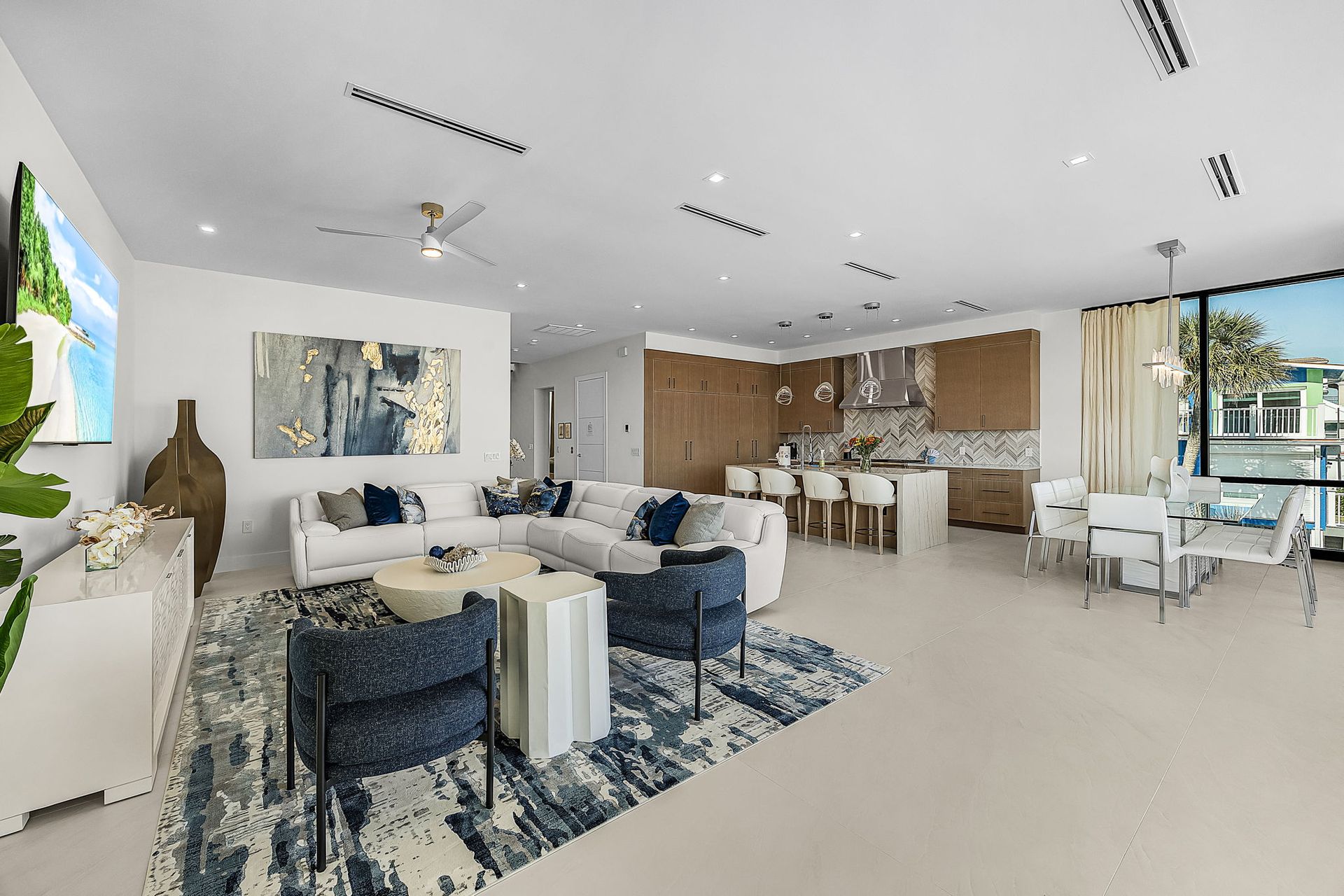 Spacious, modern living room with white walls, blue accents, and open kitchen.