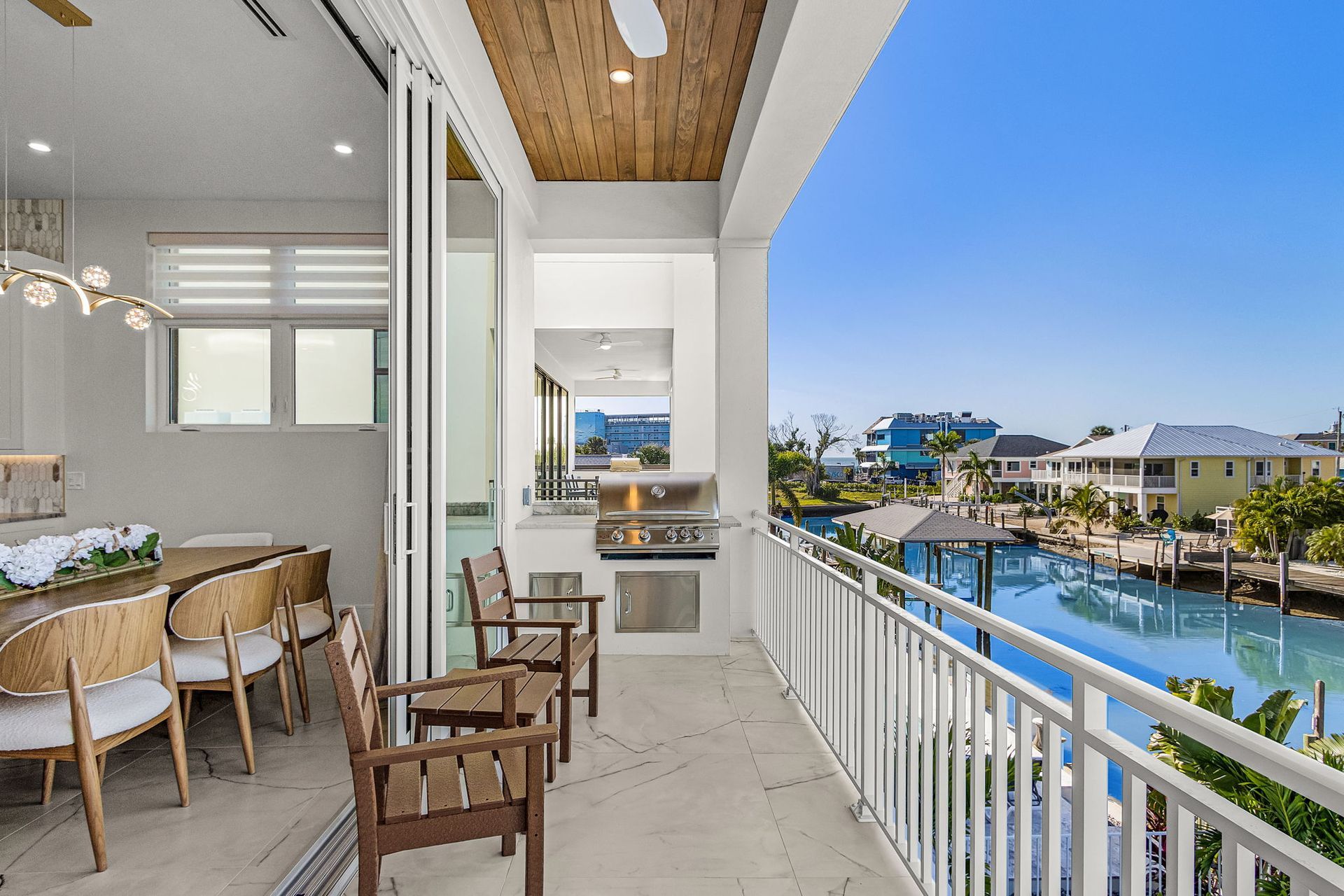 Balcony overlooking water, with seating, an outdoor kitchen, and a dining room visible inside.