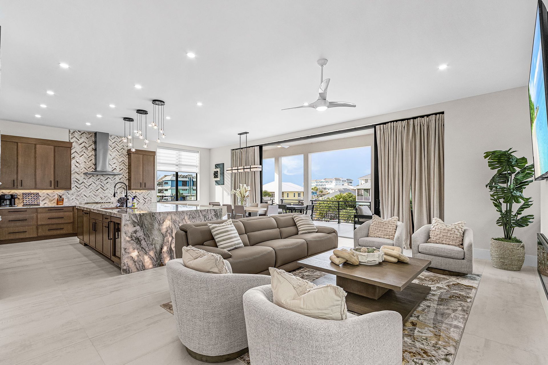 Modern open-concept living area with kitchen, dining, and seating. Large windows, neutral tones, and luxury decor.