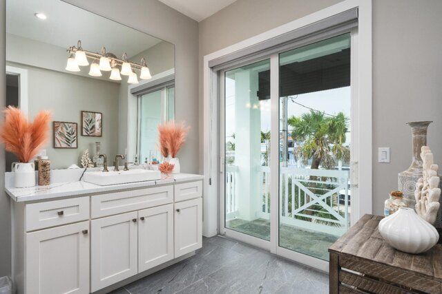 Bathroom with white vanity, large mirror, and sliding glass door to a balcony. Gray walls and flooring.