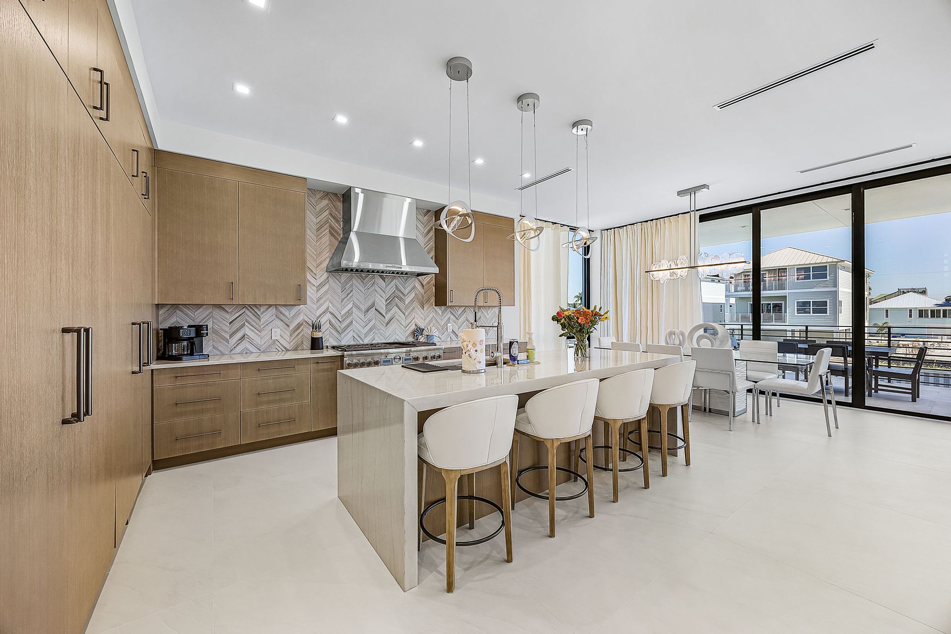 Modern kitchen with island, cabinets, marble backsplash, and large windows overlooking water.