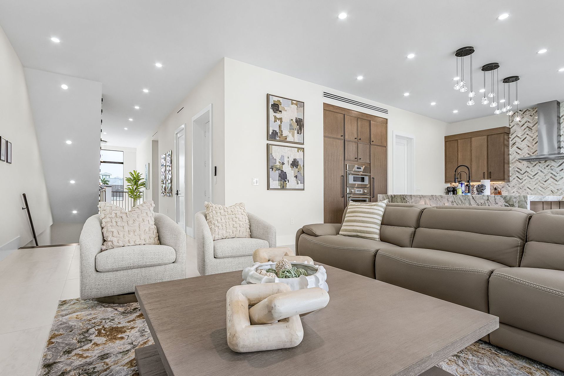 A modern living room with a sofa, armchairs, and a coffee table. Bright lighting and neutral tones.