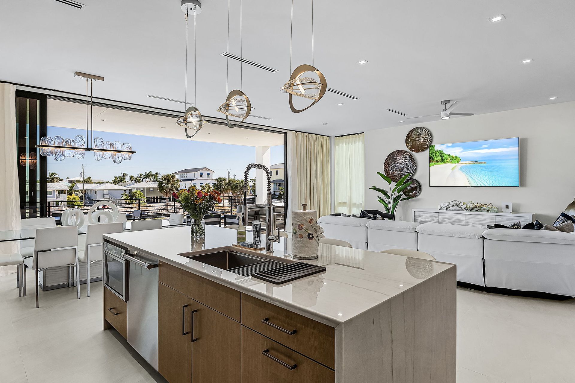 Modern kitchen with island, overlooking a canal, open sliding doors. White walls, wood cabinets, stainless steel appliances.