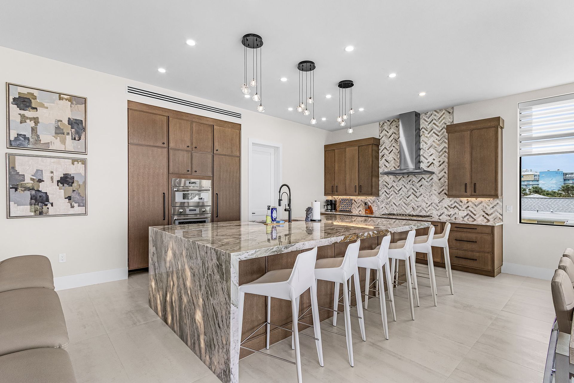 Modern kitchen with large island, granite countertop, brown cabinets, and white bar stools.