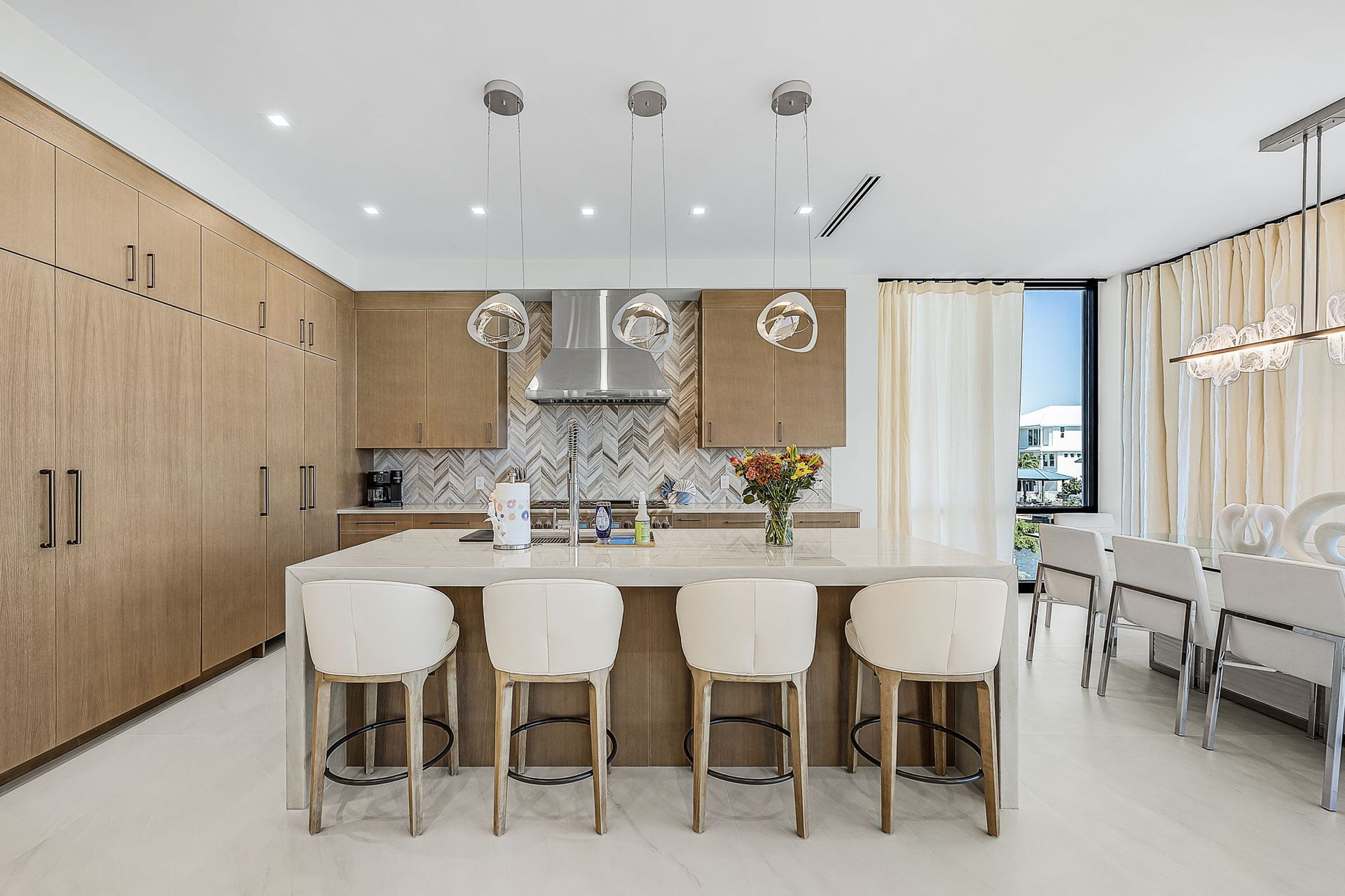 Modern kitchen with light wood cabinets, marble island, and four white stools.