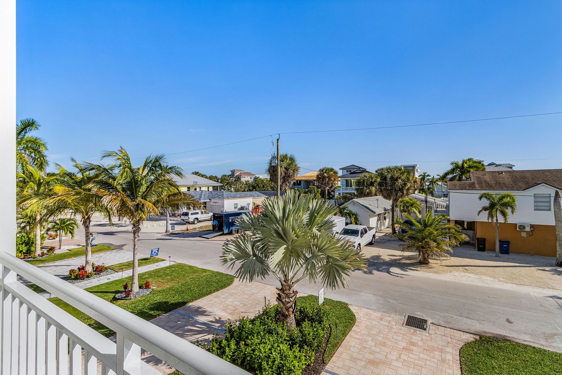 Balcony view overlooking a street with palm trees, buildings, and a clear blue sky.