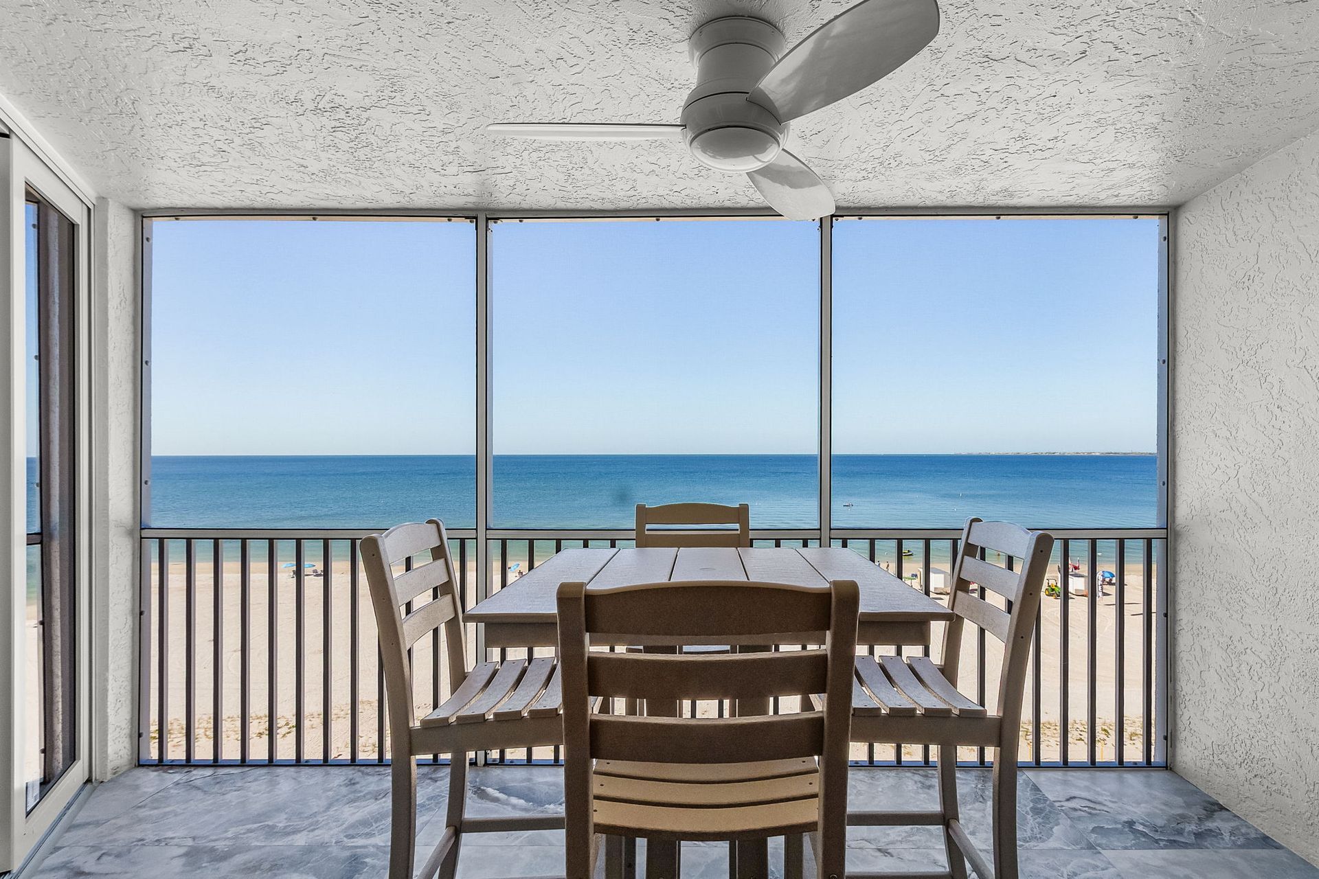 A dining table and chairs on a screened-in porch, overlooking the ocean.