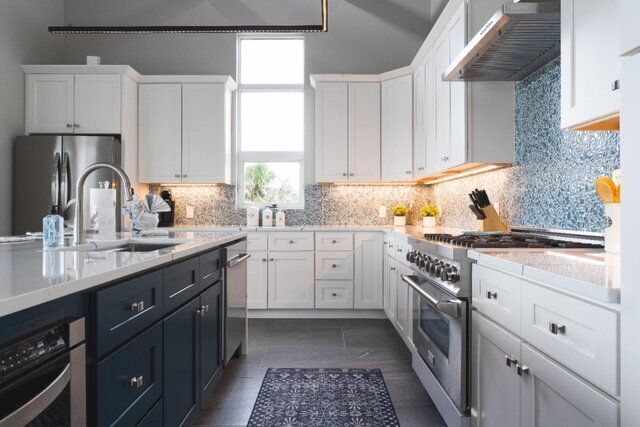 Modern kitchen with white and dark blue cabinets, stainless steel appliances, and a mosaic backsplash.